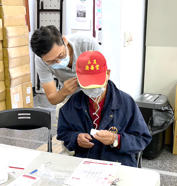 「元健助聽器高雄鳳山店」店長楊杰龍先生為受贈耳寶助聽器藍牙耳掛天籟機的民眾配戴耳機、進行使用教學。