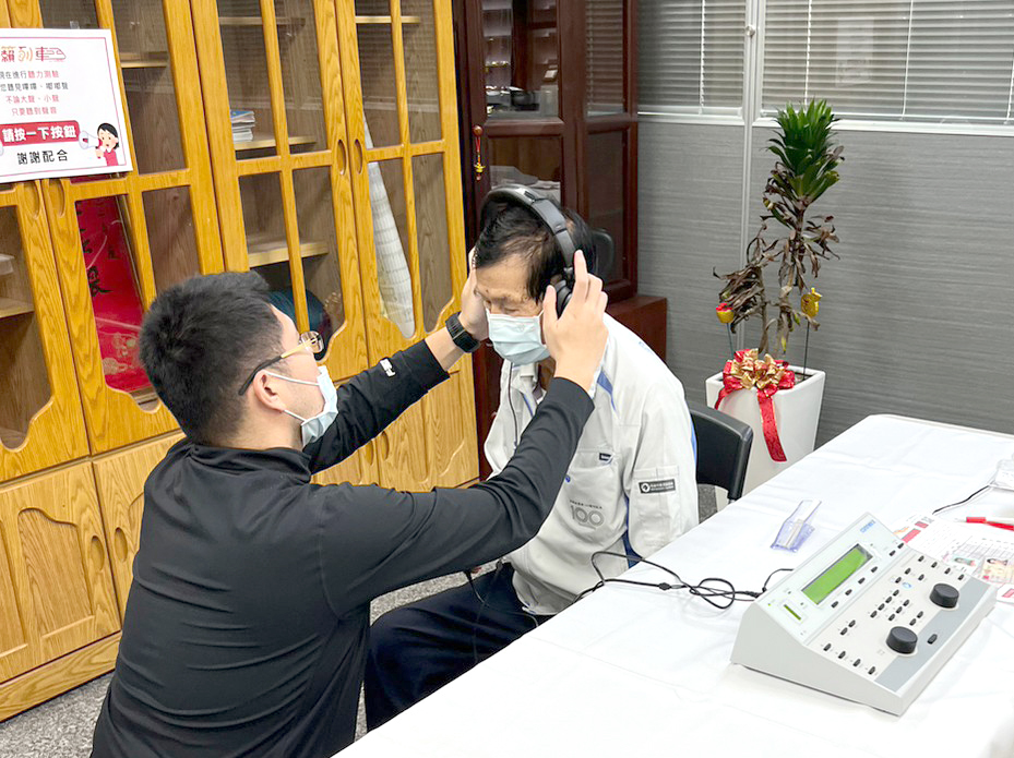 「元健助聽器高雄楠梓店」店長徐梓傑先生為接受免費助聽器適配聽力檢測的民眾配戴耳機。